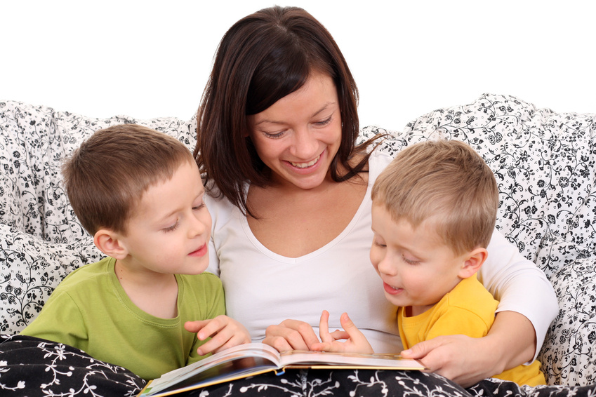 mother and two sons reading book in bed